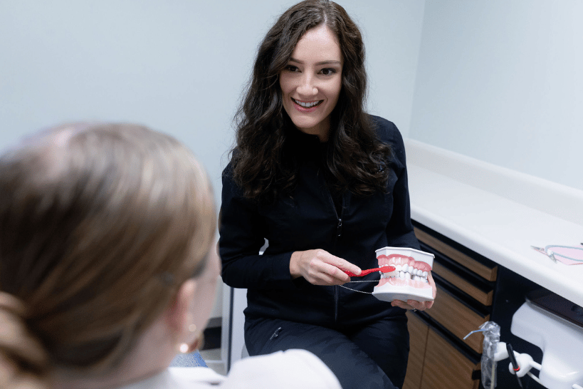 Female dentist explaining brushing technique using teeth model and toothbrush