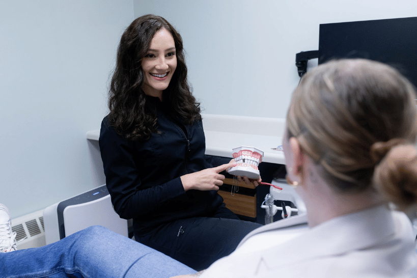 Dentist holding teeth model while teaching female patient proper brushing technique